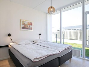 A bedroom with a bed, two bedside lamps, a hanging light fixture, a framed picture on the wall, and a view of the outside through large windows. - Spacious Apartment in RingkÃ¸bing near Sea (Ringkobing)