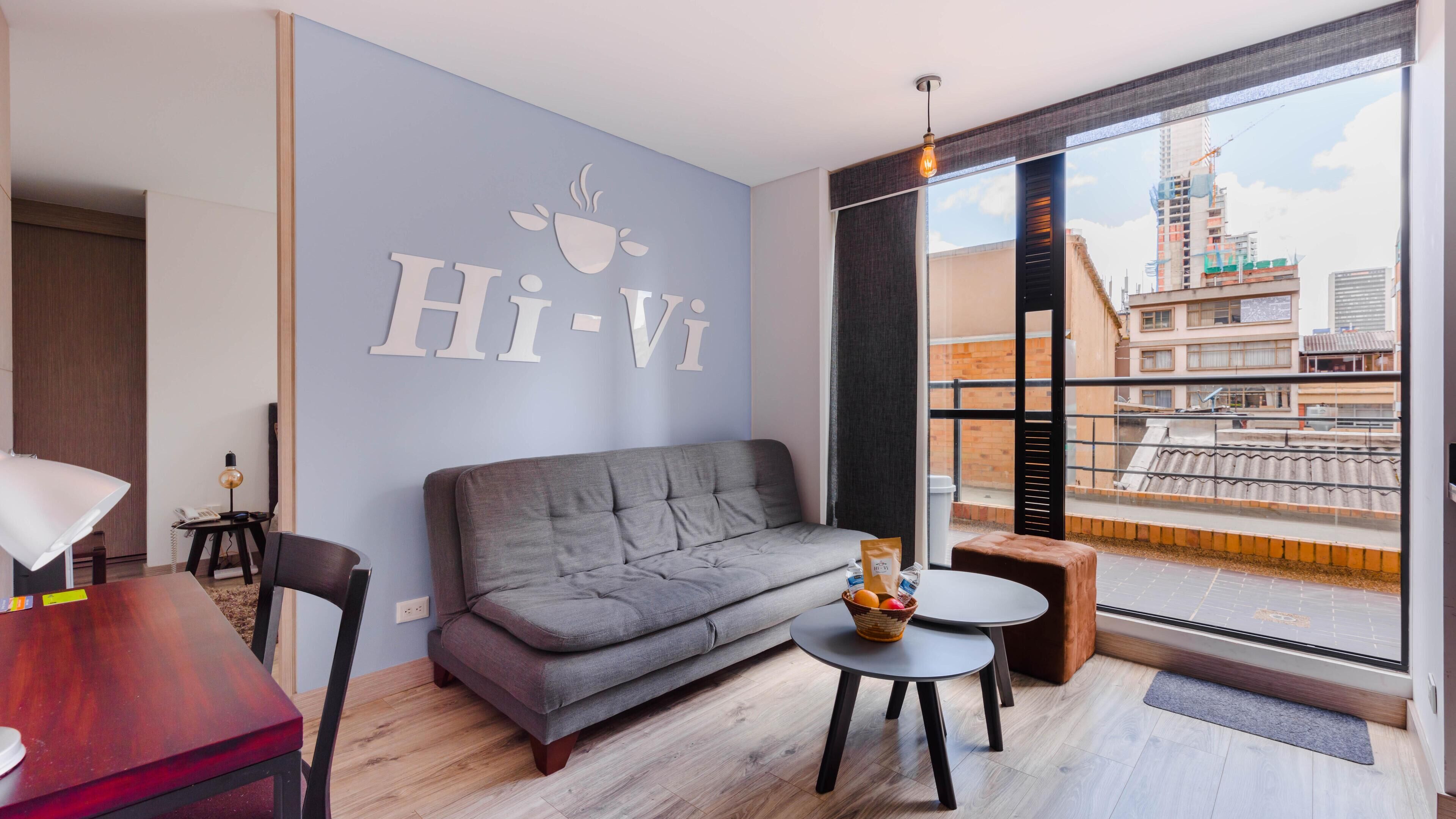 Ein modernes Wohnzimmer mit grauem Sofa, einem kleinen runden Tisch und einem großen Fenster mit Blick auf die Stadt.