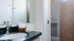 A bathroom with a black countertop, a white sink, a mirror, a glass shower enclosure, and a towel basket.