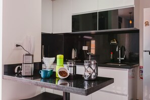 Uma cozinha com bancada preta, armários brancos e uma cafeteira de aço inoxidável.