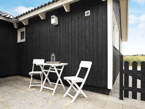 A patio with a table and two chairs, a lantern, and a small window.