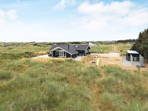 Une maison dotée d’un grand porche, d’une balançoire et d’un espace clôturé, entourée de champs verdoyants et d’autres maisons.