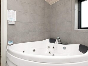 A modern bathroom with a freestanding bathtub, grey tiled walls, a window, and a water meter.