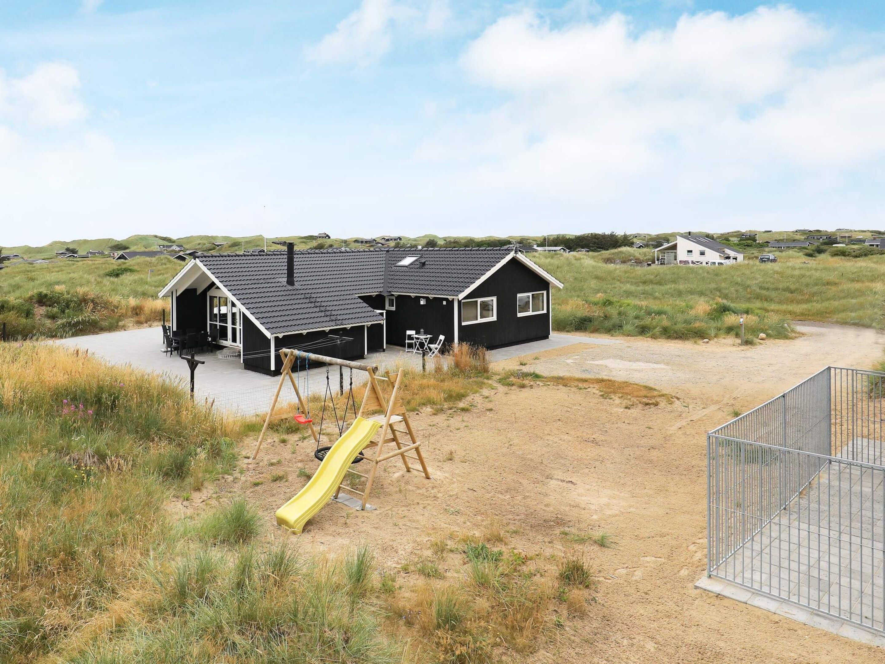 A black house with a patio and a yellow slide in a grassy area.