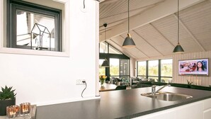 Een moderne keuken met een groot eiland, hanglampen en een televisie waarop een nieuwsprogramma wordt vertoond.