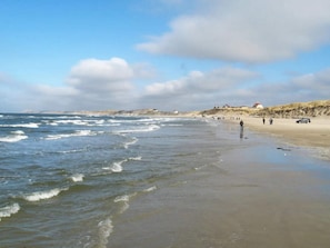 A beach with waves, people, and buildings in the distance.