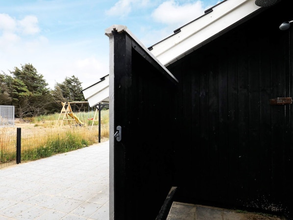 A black metal door with a latch, a concrete structure with a white roof, and a playground with a slide in the background.
