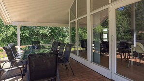 Een overdekt terras met een eettafel en stoelen, grote glazen deuren en uitzicht op een achtertuin met tuinmeubilair.
