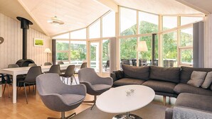 Een modern interieur met houten plafond, grote ramen, een bank, stoelen, een tafel en een open haard.