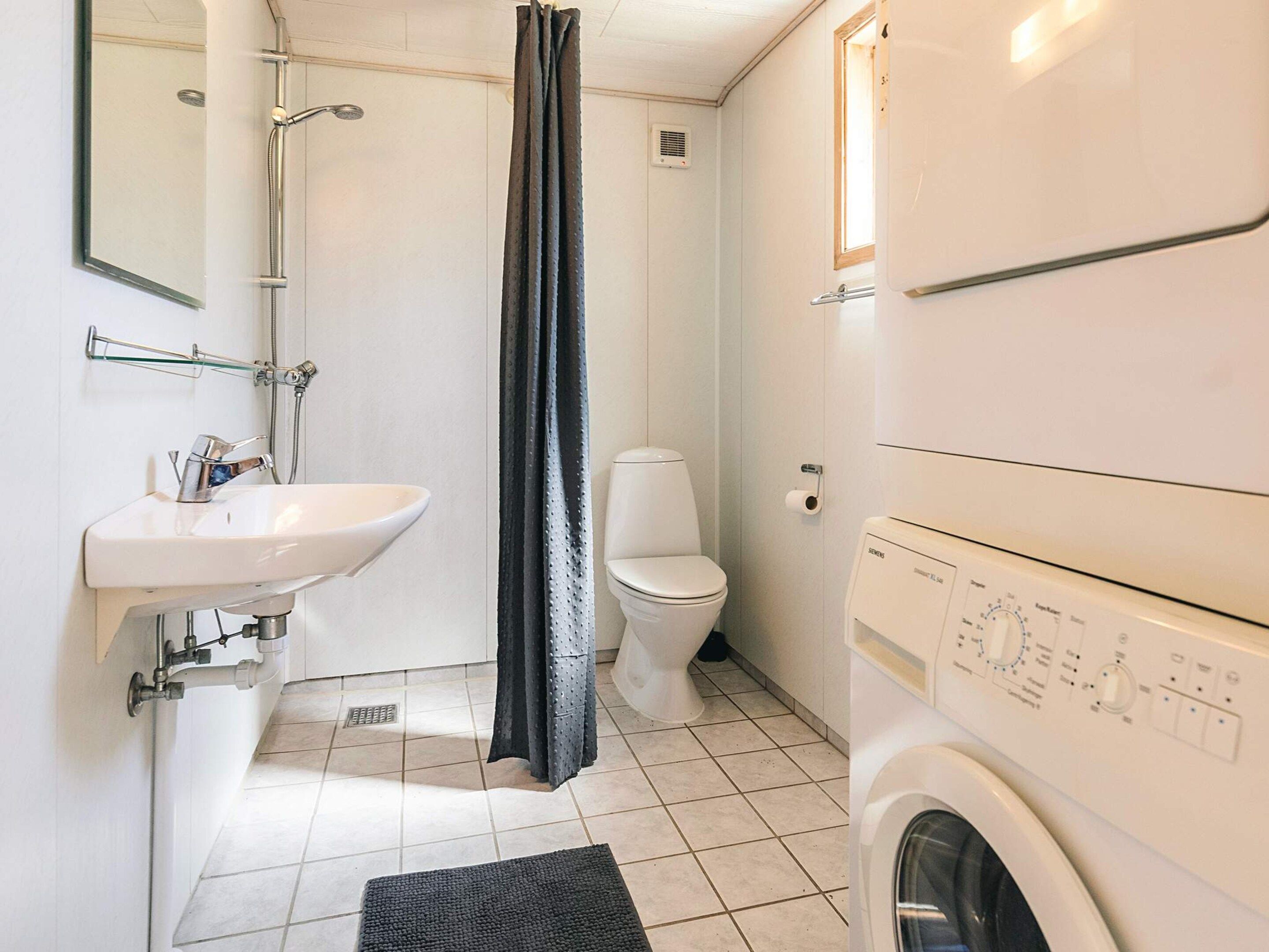 Et lille badeværelse med vask, toilet, brusebad og vaskemaskine.