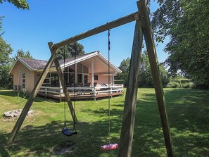 A wooden swing set in a backyard with a house in the background. - 4 Star Holiday Home in Vaeggerlose (Vaeggerlose)