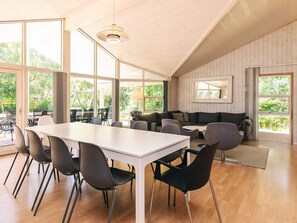 A spacious room with a large dining table, chairs, a sofa, and a window with a view of greenery. - 4 Star Holiday Home in Vaeggerlose (Vaeggerlose)