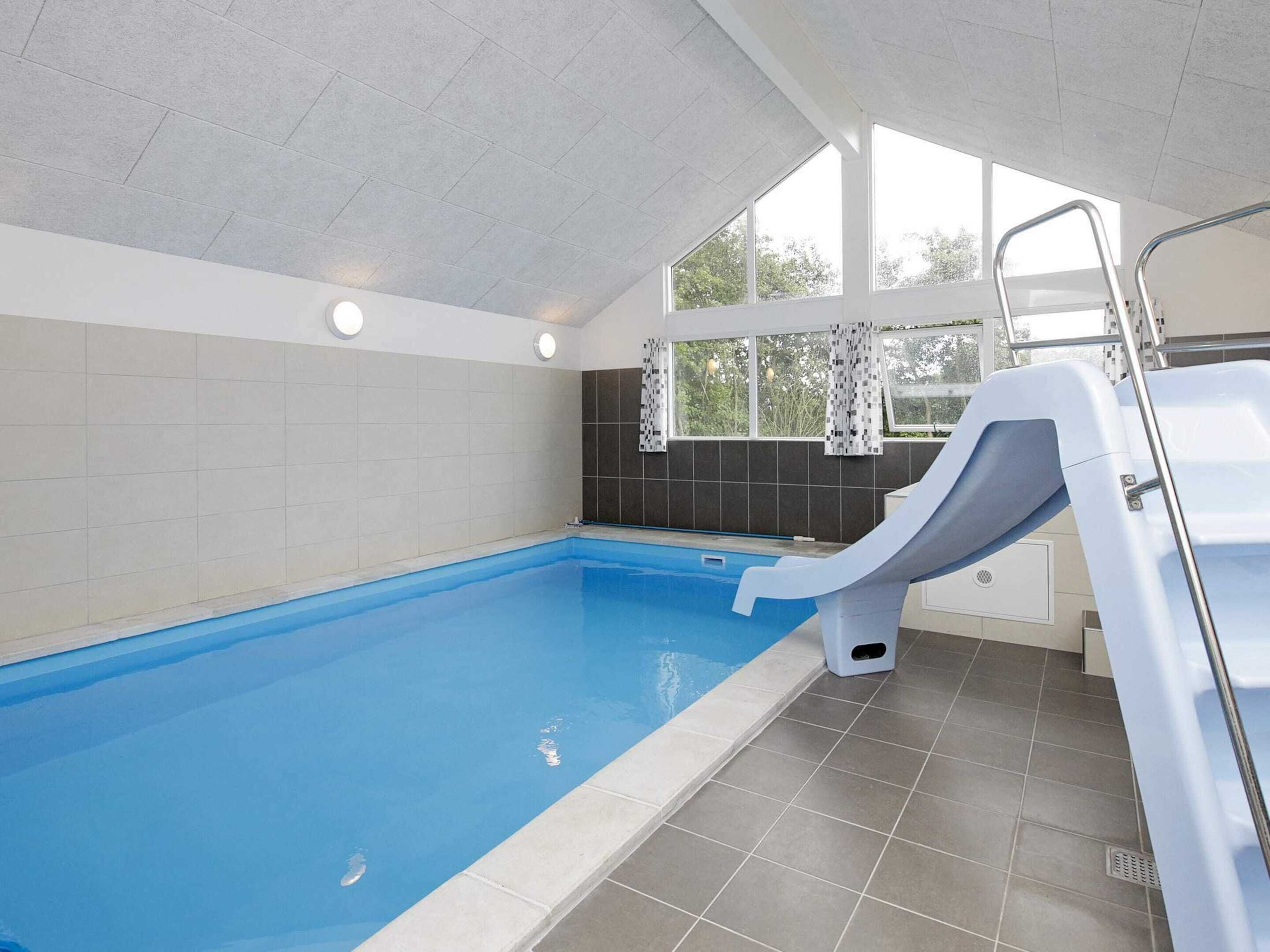 An indoor swimming pool with a slide, tiled walls, and a window with curtains.