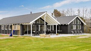 A modern house with a covered patio, a play area with a slide, and a lawn. - 5 Star Holiday Home in Blavand (Blavand)
