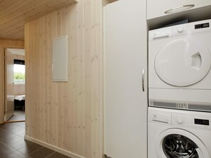 A laundry room with a stacked washer and dryer, wooden walls, and a door leading to another room. - 5 Star Holiday Home in Blavand (Blavand)