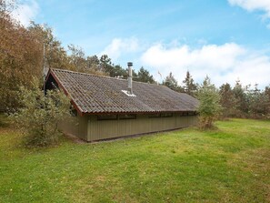 Een laag gebouw met een schuin dak, schoorsteen en een klein terras.