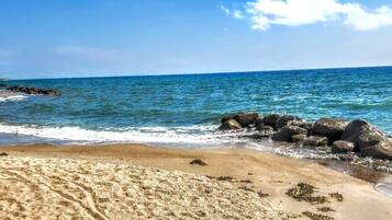 Una playa arenosa con huellas visibles y un promontorio rocoso.