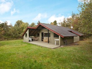 A small, single-story wooden cabin with a sloped roof, a porch with outdoor seating, and a satellite dish. - 6 Person Holiday Home in Rodby (Rodby)