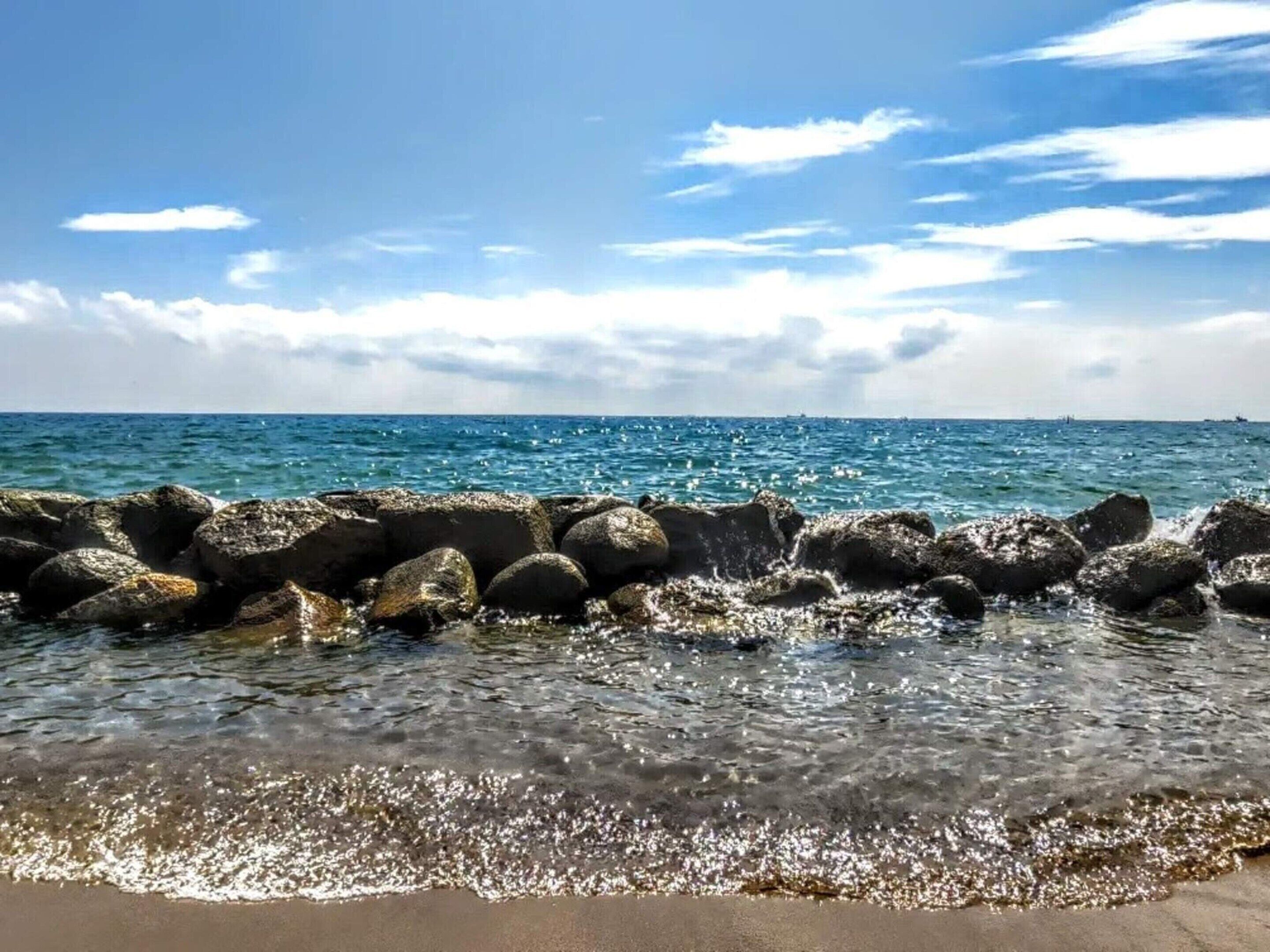 Una costa rocosa con aguas azules cristalinas y cielo parcialmente nublado.