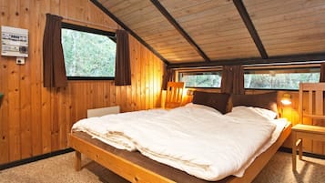 A wooden cabin bedroom with a single bed, two windows, and a nightstand.