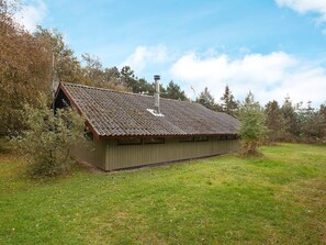 A small, single-story building with a sloped roof and a chimney, surrounded by a grassy field and trees. - 6 Person Holiday Home in Rodby (Rodby)