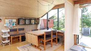 Interior acolhedor de uma cabana com uma mesa de jantar de madeira, bancos e uma grande janela com vista para o exterior.