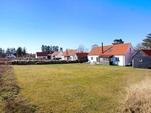 A row of houses with red roofs and white walls, a grassy field, and trees in the background.