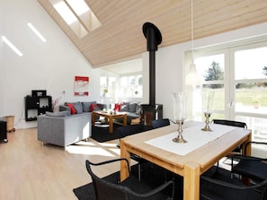 A modern living room with a dining table, sofas, a fireplace, and large windows.