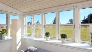 Habitació amb un sofà gris, finestres blanques i plantes en testos al davant de la finestra.