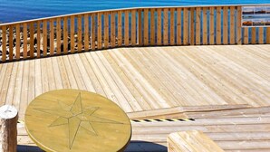 Eine Holzterrasse mit einem sternförmigen Tisch und Bänken, mit Blick auf ein Gewässer.