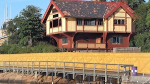 Ein zweistöckiges Holzhaus mit Balkon, gelbem Zaun und einem Steg mit einem Boot.