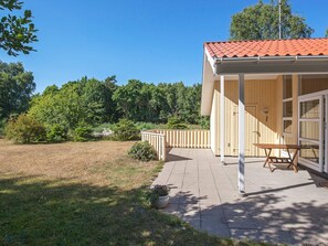 A single-story building with a covered patio, a wooden deck, and a view of a forested area. - 5 Star Holiday Home in Vaeggerlose (Vaeggerlose)