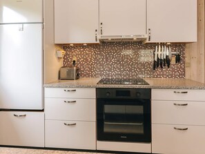 A kitchen with white cabinets, a microwave, an oven, a toaster, and a tiled backsplash. - 5 Star Holiday Home in Vaeggerlose (Vaeggerlose)