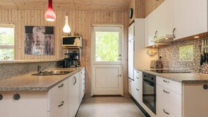 Eine Küche mit Holzwänden, einem Spülbecken, einer Kaffeemaschine und einer gefliesten Rückwand.
