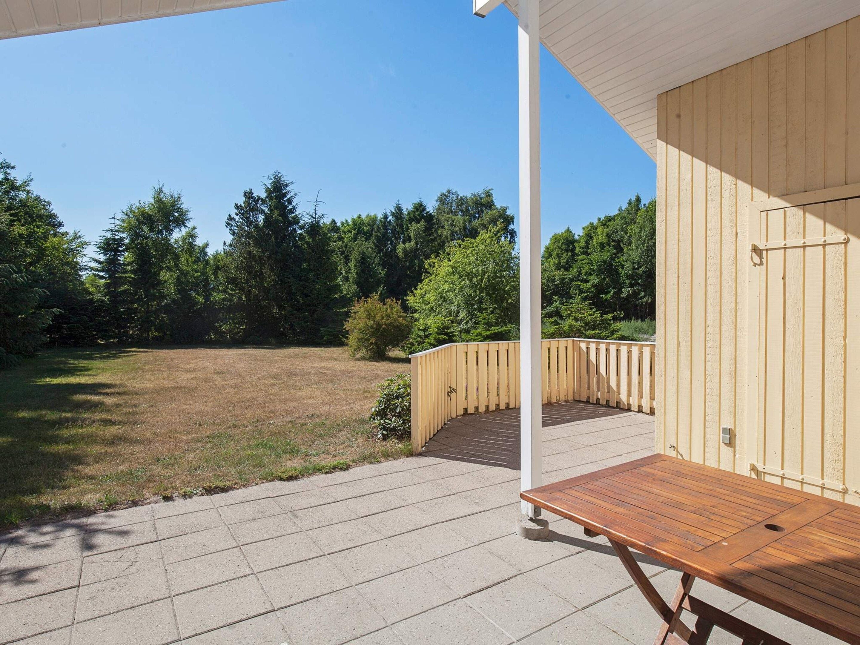 A wooden deck with a table, a white post, and a view of a grassy area with trees.