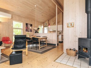A cozy interior with a dining area, a black leather chair, a wooden table, a kitchen with white cabinets, and a wood-burning stove. - 5 Star Holiday Home in Vaeggerlose (Vaeggerlose)