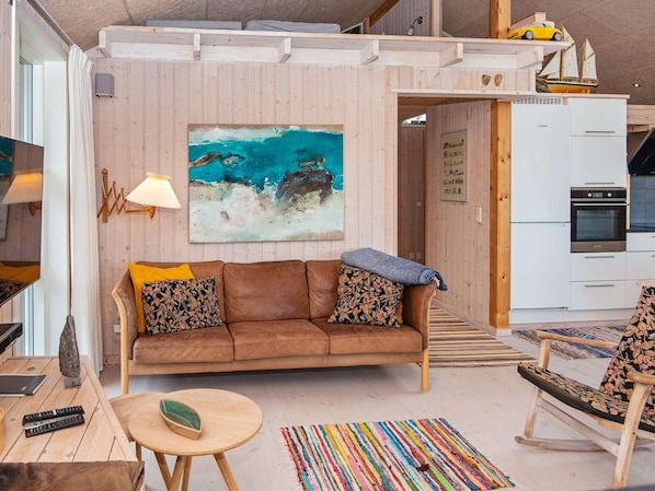 Ein gemütlicher Wohnbereich mit einem braunen Sofa, einem farbenfrohen Teppich und einer Küche mit weißen Schränken.