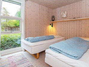 A room with two beds, a window, a wooden wall, and a small shelf with a lantern. - 5 Star Holiday Home in Glesborg (Glesborg)