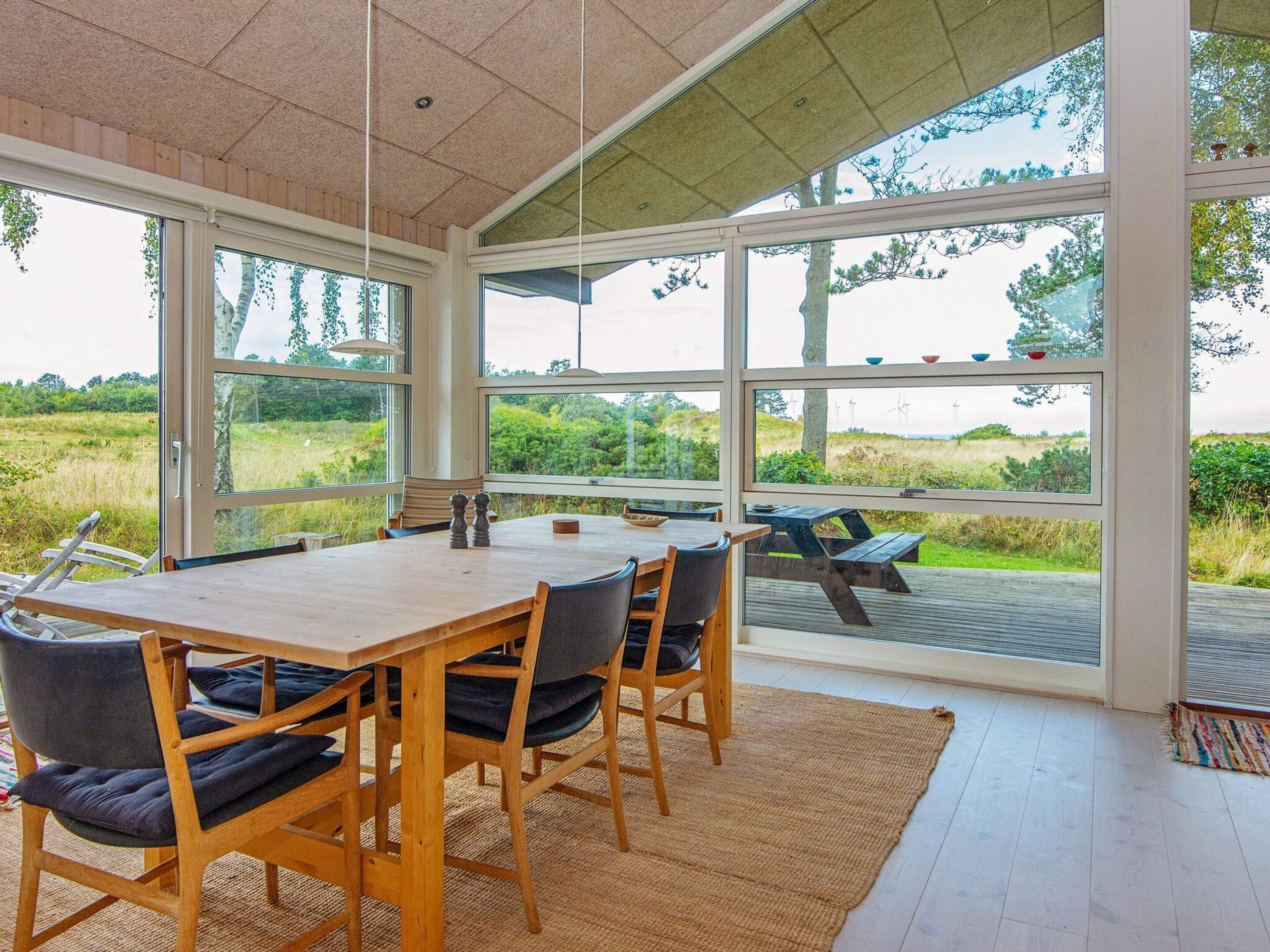 A dining area with a large table and chairs, large windows offering a view of the outdoors.