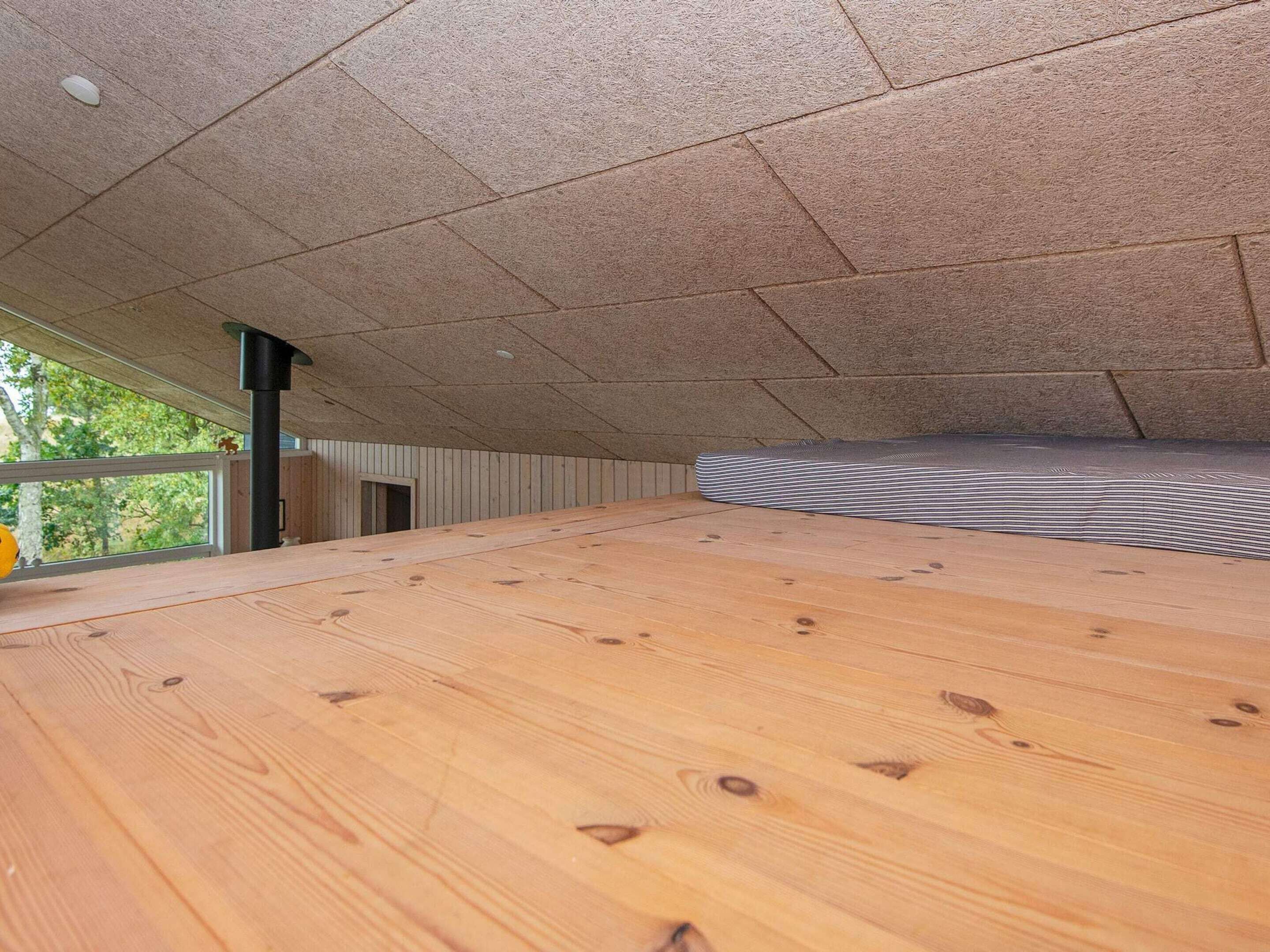 Una habitación con techo inclinado, suelo de madera y vistas a la vegetación exterior.