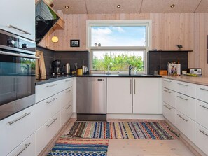 A modern kitchen with stainless steel appliances, white cabinetry, and a large window providing a view of greenery.