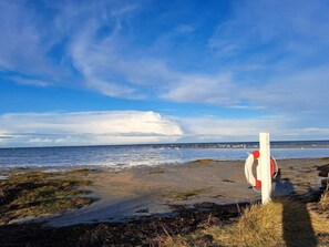 A beach with a lifebuoy attached to a post, waves in the background, and a partly cloudy sky. - 5 Star Holiday Home in Glesborg (Glesborg)