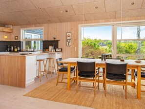 A modern kitchen with wooden cabinetry, a large island with stools, and a dining area with a view of greenery.