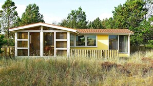 Une maison de plain-pied avec un toit en pente, de grandes fenêtres et une clôture en bois qui entoure la propriété.