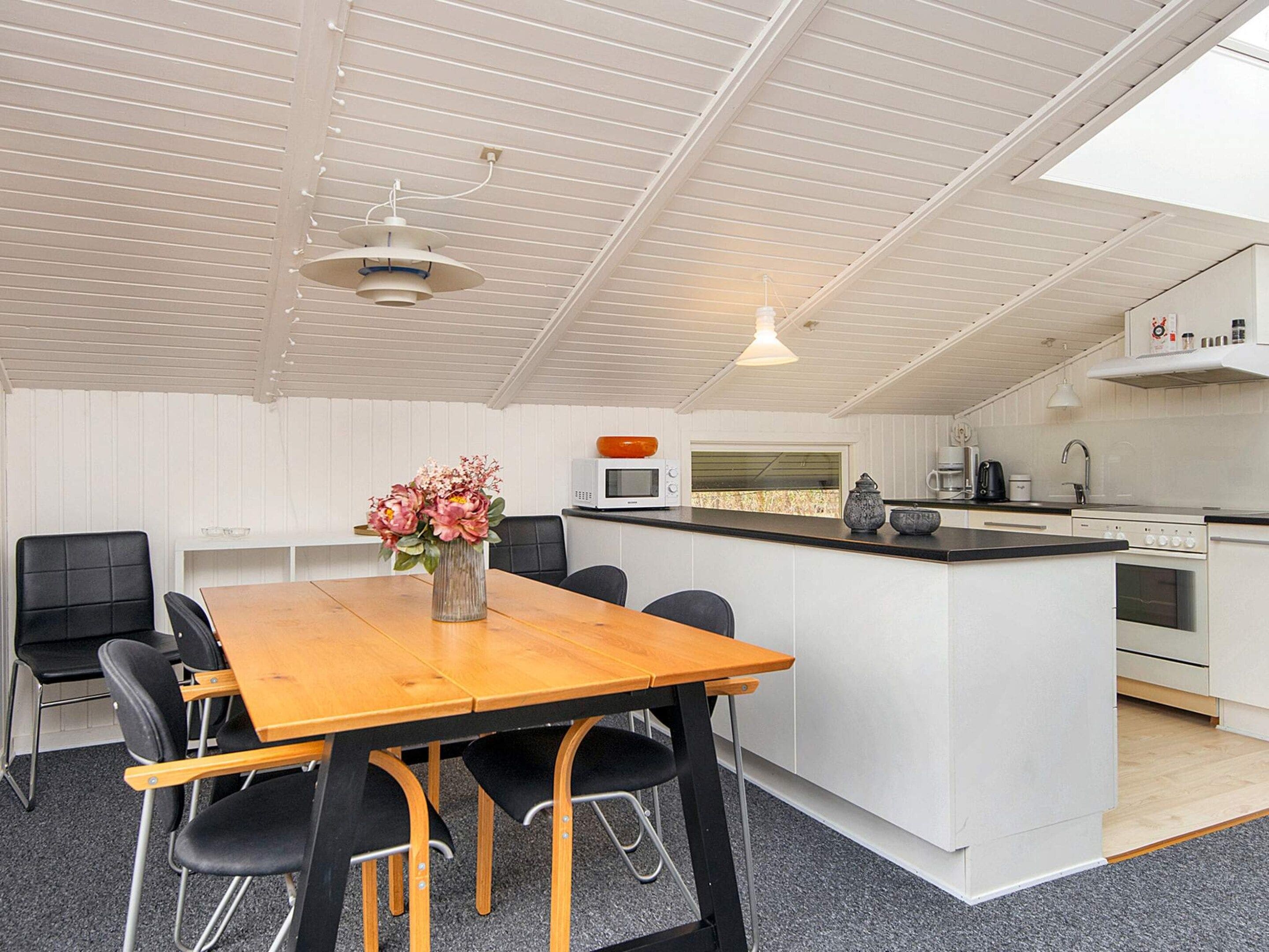 Een moderne keuken met witte kastjes, een houten eettafel en zwarte stoelen.
