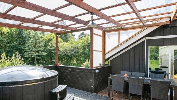A hot tub on a wooden deck with a glass ceiling, surrounded by outdoor furniture. - 4 Star Holiday Home in Ansager (Ansager)