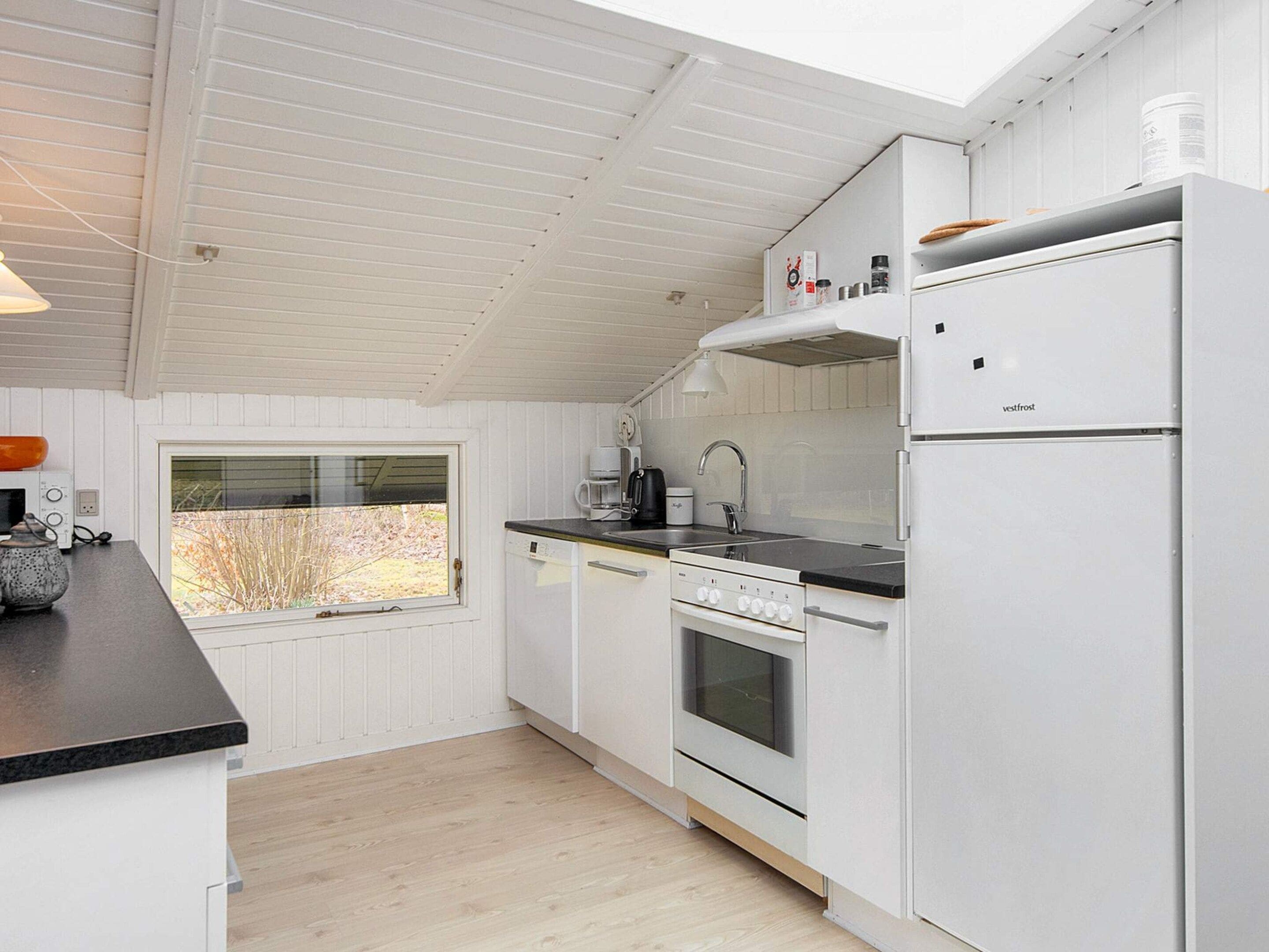 A modern kitchen with white cabinetry, a built-in oven, a refrigerator, and a window providing a view of the outdoors.