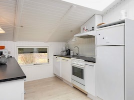 Una cocina moderna con armarios blancos, horno empotrado, refrigerador y ventana con vista al exterior.