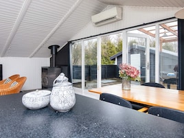 Una cocina moderna con estufa integrada, una mesa de comedor con sillas y un amplio ventanal corredera que da a un jardín.