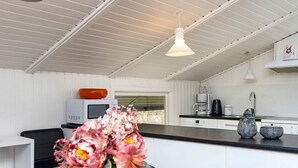 A modern kitchen with white cabinetry, a wooden dining table, and a vase of flowers. - 4 Star Holiday Home in Ansager (Ansager)